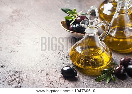 Olive oil in a glass bottle and olive branch on brown stone table