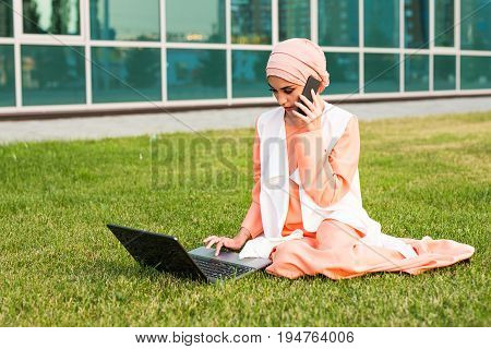 Young Muslim Woman Using Mobile Phone and Laptop In Park.