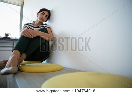 Full length of tired youngwoman by wall on seat in creative office