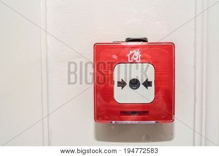 Closeup of red fire alarm box with black button on beige wall background