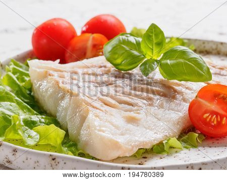 Close up view of grilled codfish with basil and cherry tomatoes in trendy white plate.