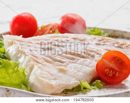 Close up view of hot grilled codfish with basil and cherry tomatoes in trendy white plate.
