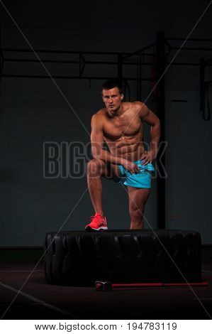 Portrait of confident young man with naked torso exersicing with hummer and tire. Weightlifting or functional training. Sports and fitness concept.