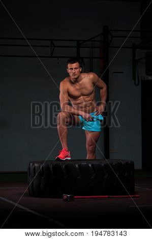 Portrait of confident young man with naked torso exersicing with hummer and tire. Weightlifting or functional training. Sports and fitness concept.