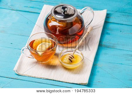 Glass cup of tea with lemon, glass teapot and honey on blue wooden table.