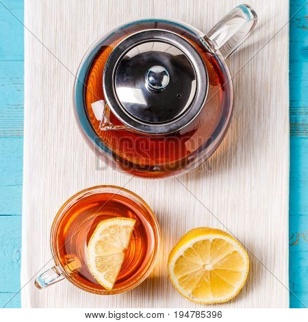 Glass cup of tea with lemon and glass teapot on blue wooden table.
