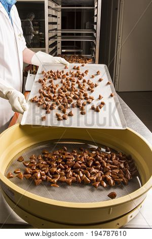 Artisanal production of caramel toffee sweets butterscotch candies. Woman with white lab coat blouse shaking separating removing the pieces of butterscotch candies traditional sweets of France