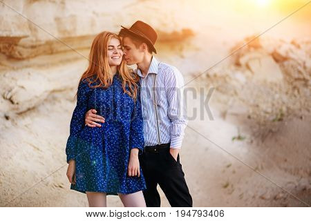 An Attractive Man Is Hugging And Kissing An Beautiful Woman In A Blue Dress In The Middle Of A Sandy