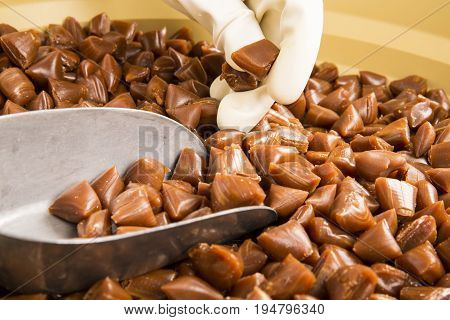 Artisanal production of caramel toffee sweets butterscotch candies. Woman with white gloves shaking put in jar get in the jugs the pieces of butterscotch candies traditional sweets of France