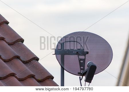 Satellite tv dish on residential home property roof. Metal mesh commercial television reception equipment.