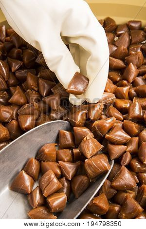 Artisanal production of caramel toffee sweets butterscotch candies. Woman with white gloves shaking put in jar get in the jugs the pieces of butterscotch candies traditional sweets of France