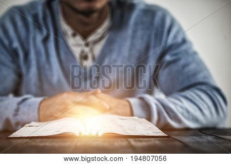 Bright spot of a flare against man with bible praying on table