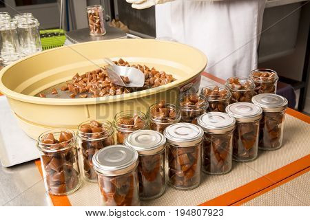 Artisanal production of caramel toffee sweets butterscotch candies. Woman with white gloves shaking put in jar get in the jugs the pieces of butterscotch candies traditional sweets of France