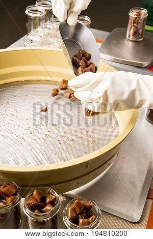 Artisanal production of caramel toffee sweets butterscotch candies. Woman with white gloves shaking put in jar get in the jugs the pieces of butterscotch candies traditional sweets of France