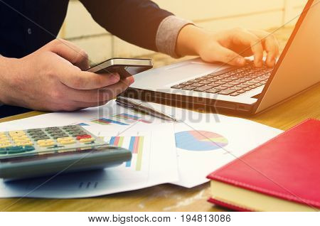 young accountant or business man using smartphone calculator with data sheet laptop on desk analyzing and calculate savings finances economy concept sunlight effect soft focus selective focus