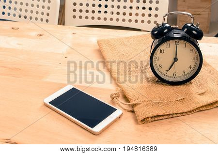 smartphone and black vintage retro alarm clock times at 7 o'clock morning on wooden desk in room selective focus copy space vintage color tone technology and working morning time concept
