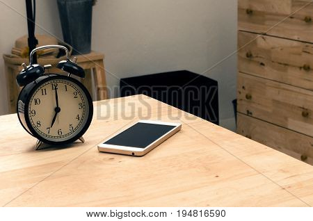 smartphone and black vintage retro alarm clock times at 7 o'clock morning on wooden desk in room selective focus copy space vintage color tone technology and working morning time concept