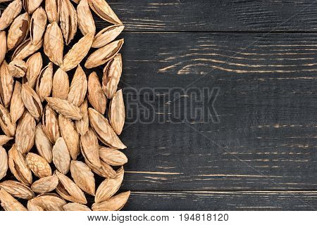 Scattered uzbek inshell almonds on an empty wooden background