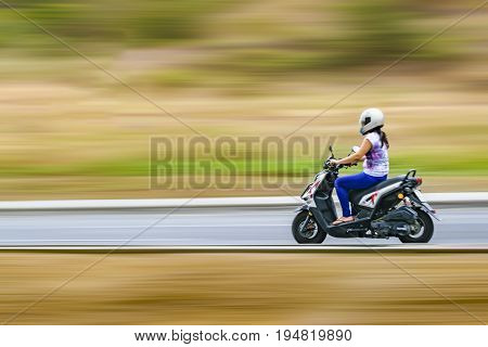 Side view shot of adult woman driving scotter at outdoor avenue