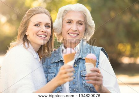 Enjoying summer together . Delighted joyful young woman enjoying the weather outdoors while expressing happiness and eating ice cream with old mother