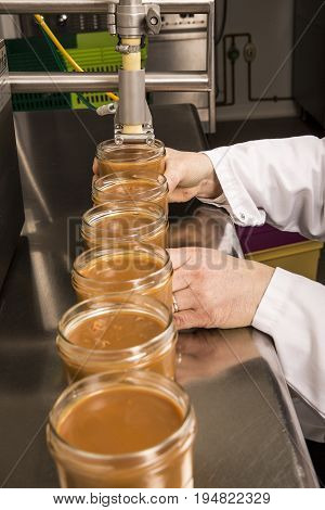 Automated food factory machine get the caramel jam in the jugs. Close up