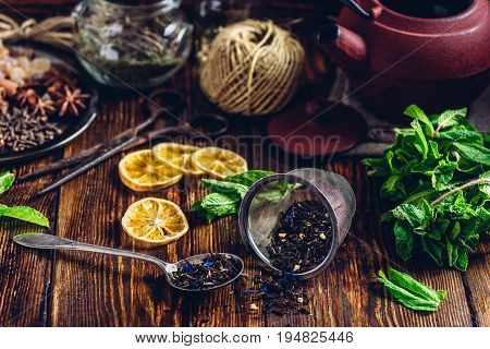 Tea in Strainer and Spoonful of Tea with Fresh Mint, Lemon Slices. Tangle with Two Jars and Teapot on Backdrop.