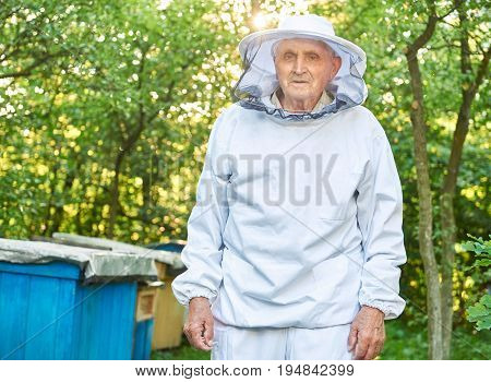Portrait of a senior male beekeeper smiling to the camera posing near a beehive at his apiary in the garden copyspace apiculture honey producing natural organic honeycraft concept.