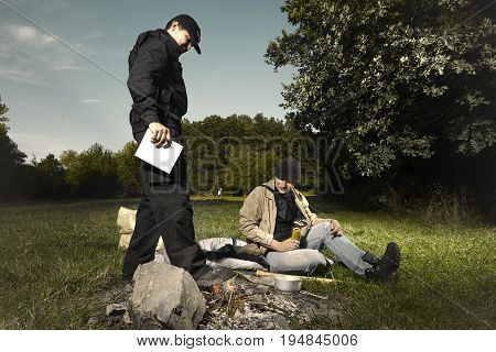 Vagabond young man checked by police patrol near illegal fireplace