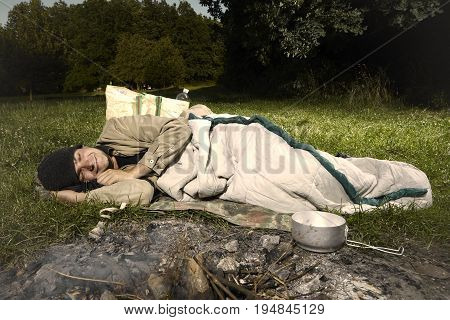 Vagabond young man sleeping in park near illegal fireplace
