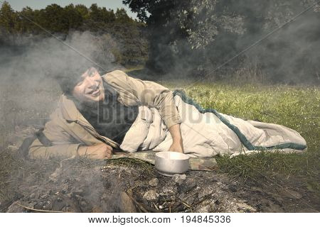 Vagabond young man sleeping in park near illegal fireplace