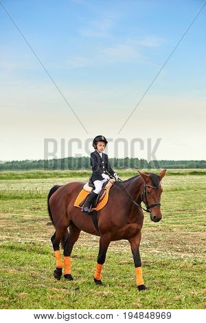 Pretty little girl jockey riding a horse across country in professional outfit