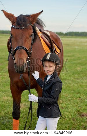 Pretty little girl jockey lead horse by its reins across country in professional outfit