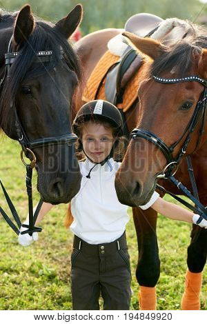 Pretty little girl jockey communicating with her horses in professional outfit