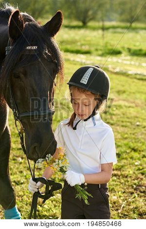 Pretty little girl jockey communicating with her black horse in professional outfit
