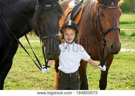 Pretty little girl jockey communicating with her horses in professional outfit