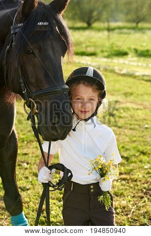 Pretty little girl jockey communicating with her black horse in professional outfit