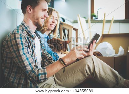 Young couple moving in new home.Sitting and relaxing after unpacking.Looking something on laptop