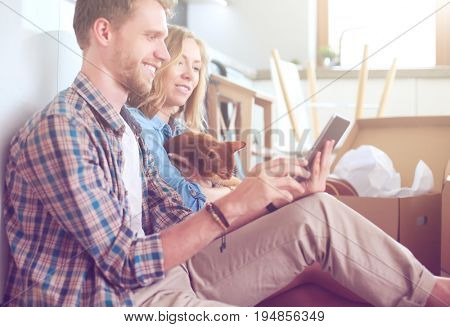Young couple moving in new home.Sitting and relaxing after unpacking.Looking something on laptop