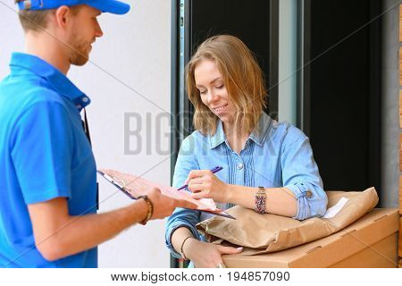 Smiling delivery man in blue uniform delivering parcel box to recipient - courier service concept