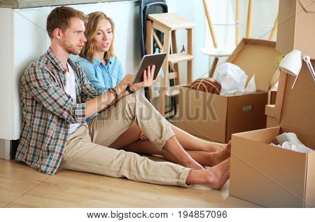 Young couple moving in new home.Sitting and relaxing after unpacking.Looking something on laptop