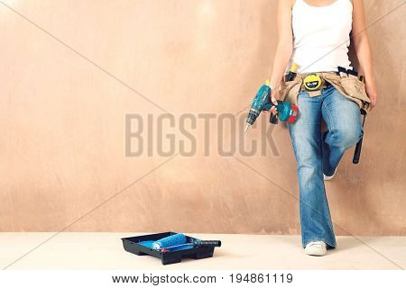 Lowsection of a young woman with toolbelt and drill leaning against wall