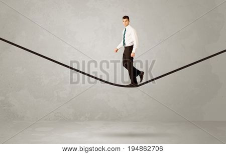 An elegan businessman in suit balancing on a tight rope with a briefcase in front of grey urban wall background environment concept