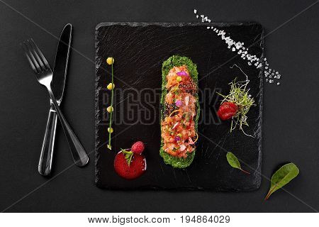 fresh salmon tartar with salt and herbs, studio shot. Fish tartar on black shale. Top view.