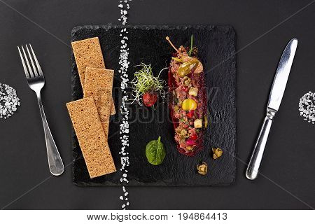 fresh beef tartar with salt and herbs and Crispbread, studio shot. Meat tartar on black shale. Top view