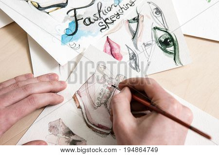 Fashion sketch in process of design. Unrecognizable man or woman draws a footwear model on desk