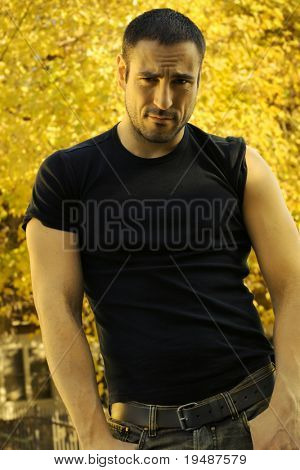 Full body moody portrait of a sexy man with sleeves rolled up against blurred natural background in golden light