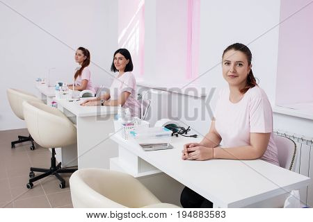 Beautician team in salon interior. Three women sits at manicure workplace
