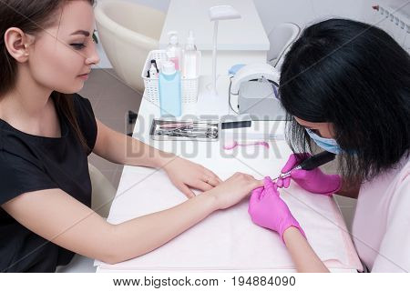 Hardware manicure in modern beauty salon. Beautician doing beauty procedure for client, professional workplace on background