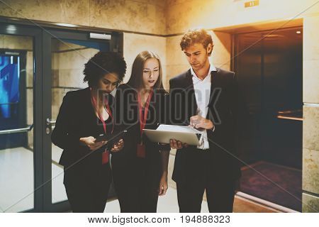 Man in formal suit sharing to his both female colleagues (young afro american probationer with digital pad and attractive caucasian woman) new presentation before business meeting via modern laptop
