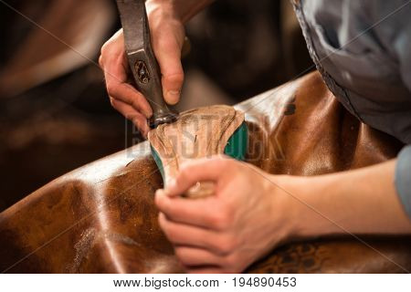 Cropped image of bootmaker sitting in workshop making shoes